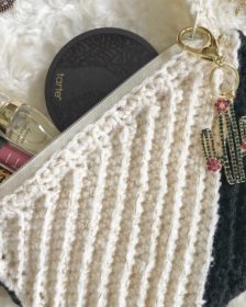 Black and white crochet clutch made with the Kelsi Clutch pattern with a cactus keyring and filled with makeup