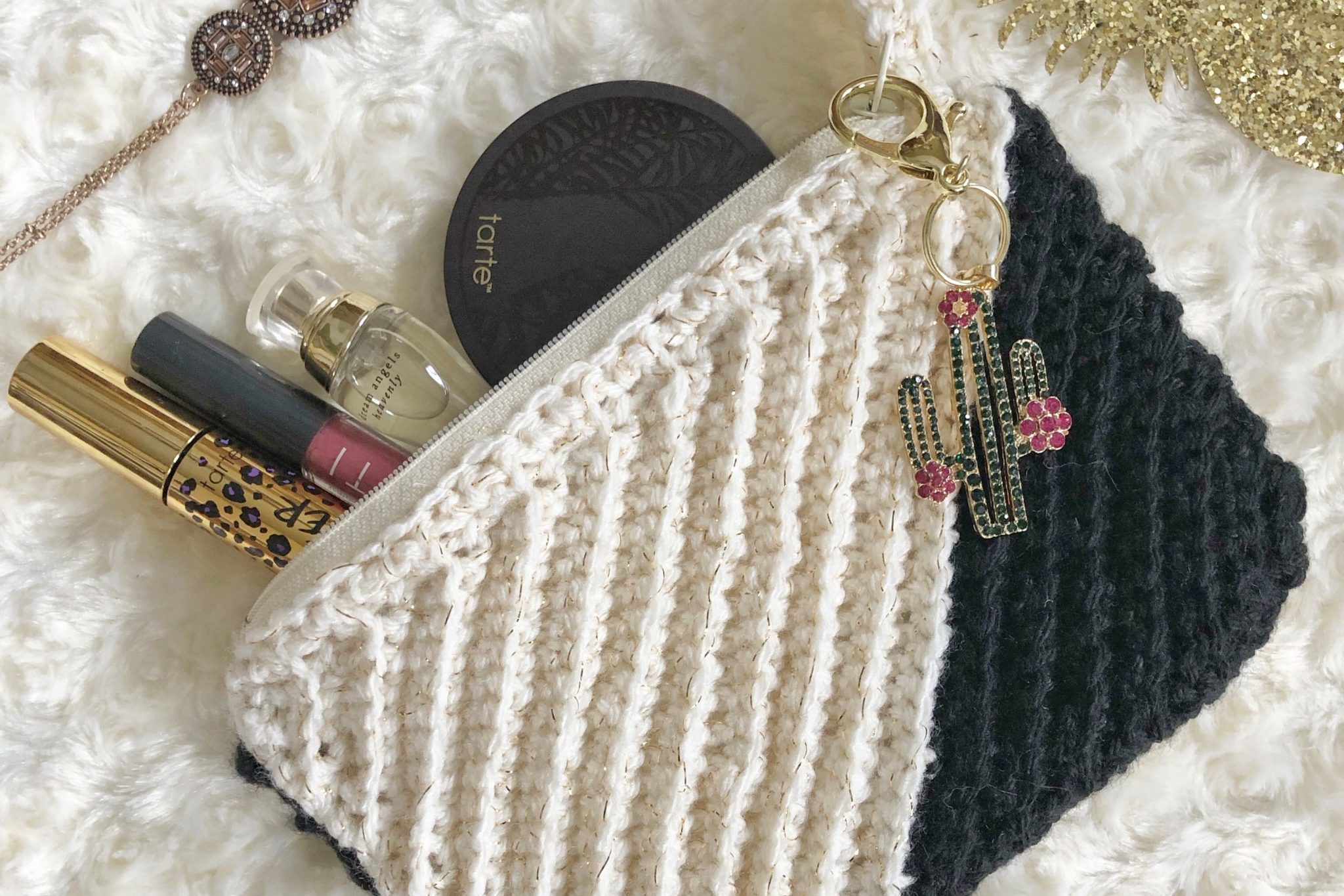 Black and white crochet clutch made with the Kelsi Clutch pattern with a cactus keyring and filled with makeup